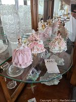 Front view of the four Dresden porcelain figurines on glass shelf, showing detailed fabric dresses and porcelain craftsmanship.