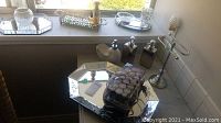 Full view of assorted bathroom items on a surface with window background showing mirrored trays, soap dispensers, glass bottles, and a small metal and glass stand.