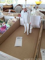 Porcelain figurine of Sir Winston Churchill in white suit, standing upright with cane and white top hat, surrounded by other figurines in background.