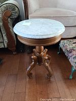 Front side view of the small round marble top table showing the white marble surface and wooden pedestal base with curved legs.