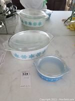 Two Pyrex glass casserole dishes with snowflake patterns and glass lids on a kitchen counter.
