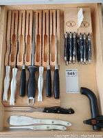 Overview: 7-slot block with Cutco white-handled knives and black honing steels, two small Laguiole blocks, six folding Laguiole pocket knives, carving fork, two white-handled Laguiole carving knives, serrated carving knife, manual sharpener