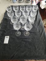 Fourteen clear crystal wine glasses with etched floral and diamond pattern, arranged on a dark cloth showing all pieces.