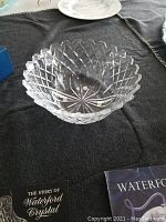 Clear Waterford crystal rose bowl on dark fabric background with 'The Story of Waterford Crystal' and Waterford informational booklets underneath.
