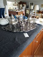 Full view of silver plated tea service on long engraved tray on grey cloth showing all five pieces.
