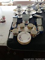 Wide view of lot on table showing Royal Worcester egg coddlers in boxes at rear, Queen's fruit‐pattern cups front center, and Duchess Tivoli cups with saucers behind