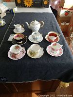 Overall view of six tea cup & saucer sets plus teapot and creamer on black cloth