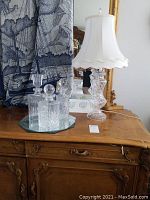 Three crystal decanters and vintage crystal lamp on wooden surface with mirror and textile background