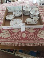 Overall set of Royal Albert petite point china laid out in two trays showing cups, saucers, plates and cream/sugar with tray.