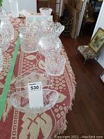 Photo of the full crystal glassware lot on a red-patterned tablecloth, showing multiple items including a vase, bowls, and napkin holder arranged together.