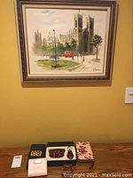 Framed cityscape painting with five purses displayed below on a table: two black purses, one floral patterned purse, one light pink compact purse, and a box with smaller patterned pouches