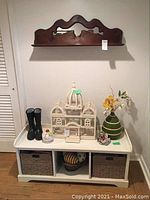 White wooden storage bench with three compartments; two containing woven baskets and one with small basket; assorted decorative items on top not included.