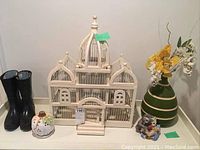 Full lot view showing black boots, white bird cage, green vase with flowers, ceramic pumpkin container, and small figurine