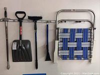 Snow shovel, broom, small brush, ice scraper, and folded lawn chair hanging on wall
