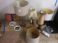 Wide view showing five lamps with various shades, three colored decorative tiles, and hardware items including a white plate with hardware and gray plastic brackets.