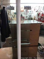 Image of two upright clear glass shower door panels with metal attachments for mounting and metal handles visible, positioned indoors with various items in the background.