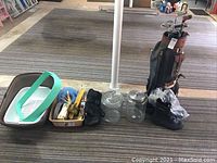 Golf bag with clubs, black boxing gloves, two clear storage jars, shallow plastic kitty litter box, and small household items on floor