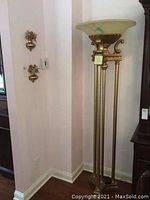 Photo showing full view of the alabaster floor lamp with gilded metal and brass detailing alongside two brass wall sconces with faux flowers mounted on the adjacent wall.