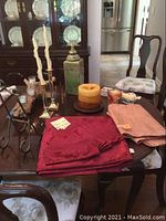 Photo of dark wood dining table with various items including fabric linens, candles, urn and trinkets