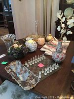 Overview of the items on a wooden table showing vase, decanter, glasses on tray, glass chess set, candleholders, coasters, and decorative vases
