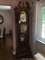 Full view of the tall case clock showing wooden case, glass front door, weights, pendulum.