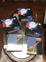 Set of 5 hardcover children's books on table, 3 titled 'Secrets of the Universe' and 2 titled 'Wildlife Fact File' with giraffe cover.
