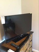 Black Samsung flat screen television on its stand with remote placed nearby on wooden surface, showing size and overall physical condition.