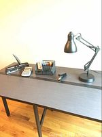 View of entire lot on dark wood desk including articulating arm lamp, stapler, calculator, hole puncher, and pens/highlighters in desk organizer