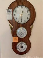 Full view of the wooden wall clock featuring clock, barometer, and thermometer with brass detailing.