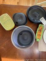 Photo of Tupperware containers with lids in yellow, gray, and black/dark colors on wooden table.