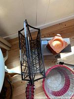 Overhead view showing black metal magazine rack with lattice sides and handles, white round table underneath, orange woven basket, tripod stand partially visible.
