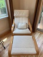 Front view of white cushioned wood framed chair with matching footstool and small pillow on chair