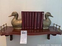 Brass duck bookends holding Webster reference set on wooden shelf.
