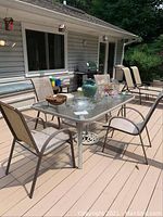 Outdoor rectangular glass-top table with four mesh chairs around it on a wood deck