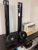 Two black tower fans, two small black desk fans, and one white window air conditioner unit on a table.