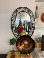 Photo of oval mirror with leaf frame and large colorful decorative bowl in front