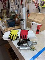 Photo of vases, tools, hardware, gloves, and a wooden mantel piece on a workbench