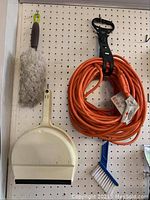 Tools hanging on peg board showing duster, dust pan, orange extension cord, and several smaller tools.