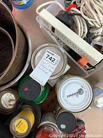 Photo shows a cluster of metal cans containing fluids, a white power strip with plugs inserted, and loosely coiled white cords. Small tubes and containers with chemical content are visible including a can displaying Zinsser branding.