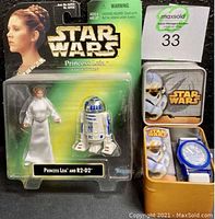Photo of original 1997 Princess Leia and R2-D2 action figure card sealed in package alongside Star Wars blue-striped R2-D2 watch in tin.
