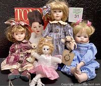 Group photo of five dolls including two porcelain Boyds dolls each holding teddy bears, Ashton Drake porcelain baby doll in blue gingham dress, pink angel ballerina musical doll, and Tonner Doll catalog with brunette doll on cover.