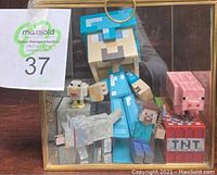 Photo showing full set of Minecraft collectible figures inside a glass display case including a large Steve figure, a wolf, pig, chicken, a smaller Steve figure and TNT block.