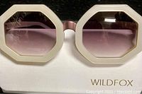 Front view of the octagon-shaped Wildfox sunglasses with a thick ivory/off-white frame and rose gold gradient lenses displayed on the white stand with Wildfox branding.