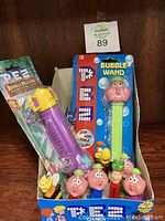 Full box view of multiple PEZ dispensers including bubble wand and syringe novelty dispenser