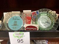 Photo showing two vintage Las Vegas glass ashtrays including Tropicana and MGM Grand, with matchbooks behind them.