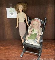 Two vintage dolls, one seated porcelain baby doll in rocking chair and one standing doll.