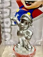 Close-up of the silver Mario amiibo figurine inside its clear plastic packaging showing the front and detail of the figure.