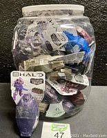 Large clear plastic jar filled with sealed Mega Bloks Halo figures on card in assorted colors.