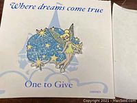 Photo of the Tinker Bell collectible pin on decorative backing card with text 'Where dreams come true' and 'One to Give'. Glittery blue star and stars behind Tinker Bell figure.