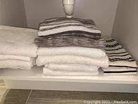 Stack of assorted bathroom towels in white, gray, and black patterns on shelf
